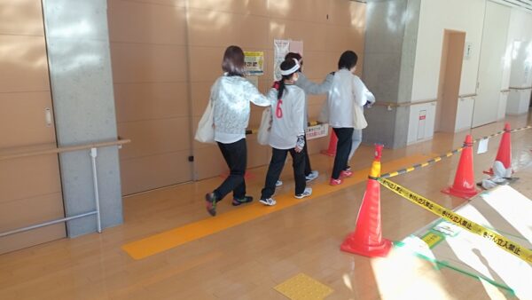 誘導マットの上を歩く3人の女子選手。その横には三角コーンで仕切られた工事資材置き場、