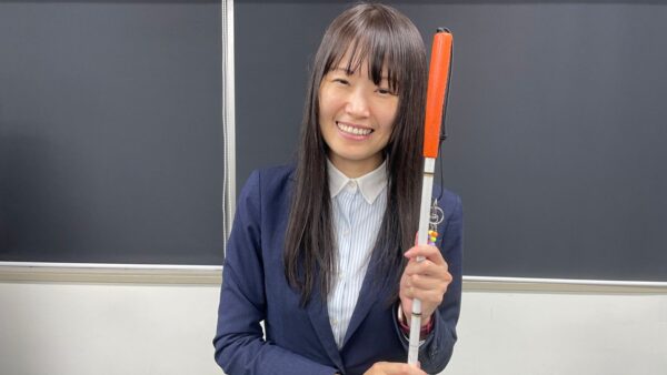 白杖をもち笑顔で写真撮影に応える杉本梢さん