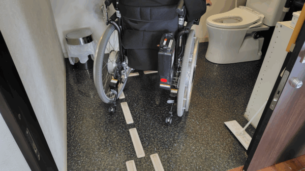 多機能トイレ内に敷かれたガイドレットの上を車椅子が通る様子。