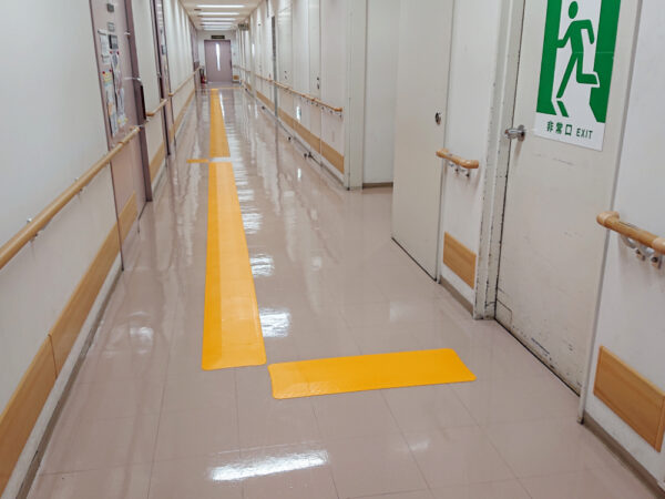 長く延びる廊下の中央付近に一直線に誘導マットが設置されている写真。誘導マットは非常口につながっている。