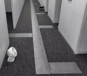 オフィス内廊下に誘導マットを設置している写真。黒に近いグレーのかーぺットの上に、グレーの誘導マットが設置されている。廊下の左右には部屋があり、それぞれ誘導マットで分岐を作っている。