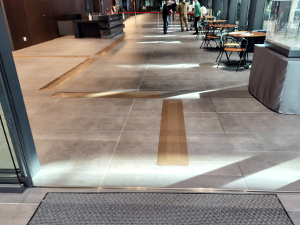 市役所入口から受付までに誘導マットが設置されている写真。入口正面の休憩スペースを避けるように、クランク状に茶色の誘導マットが設置されている。